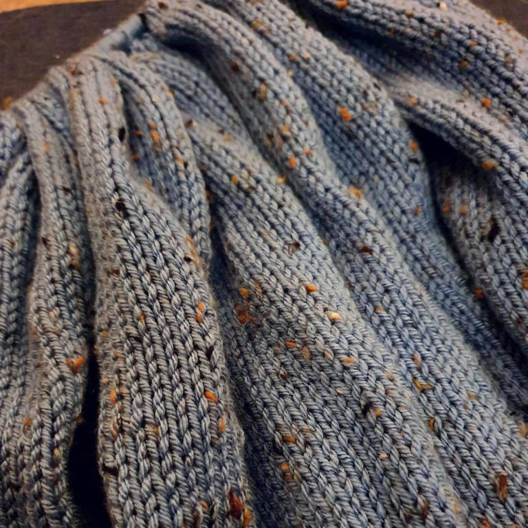 Community and Social Media about knitting A knitted blue blanket in stocking stitch, still on the needles.
