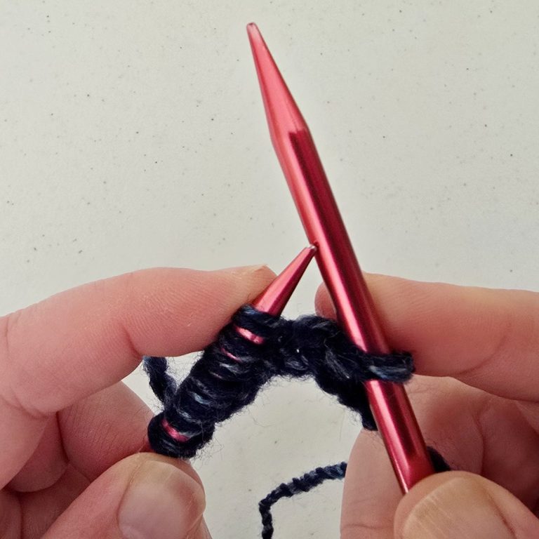 Knitting instructions A hand holding pink knitting needles with dark yarn in progress.